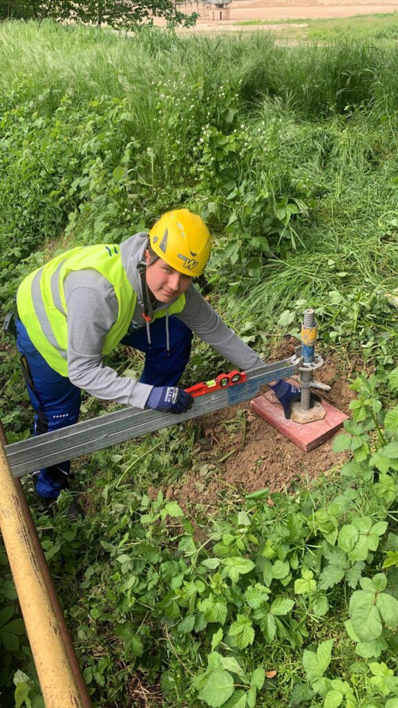 E-Waher Praktikant mit Wasserwaage beim Aufbau eines Gerüsts